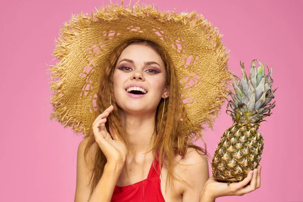 Frau mit Pistole in den Händen eines Strohhuts helles Make-up exotische Früchte Sommer rosa Hintergrund — Stockfoto