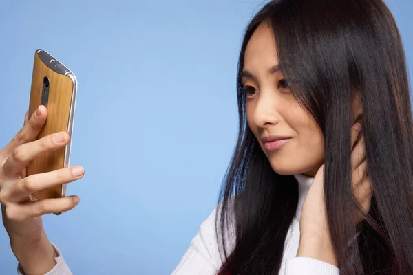 Mujer asiático apariencia teléfono en mano comunicando internet azul fondo — Foto de Stock