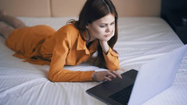 Kadın yatak odasında yatar dizüstü bilgisayarın önünde çalışır.