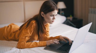 Kadın dizüstü bilgisayarın önünde yatağa uzanıyor. Serbest iş interneti.