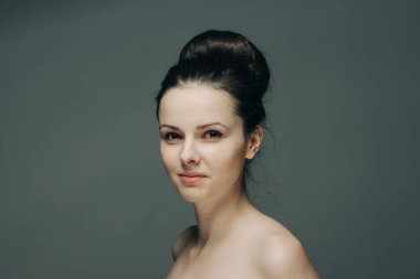 Gri arka planda gülümseyen güzel bir kadın. Çıplak omuzlar.