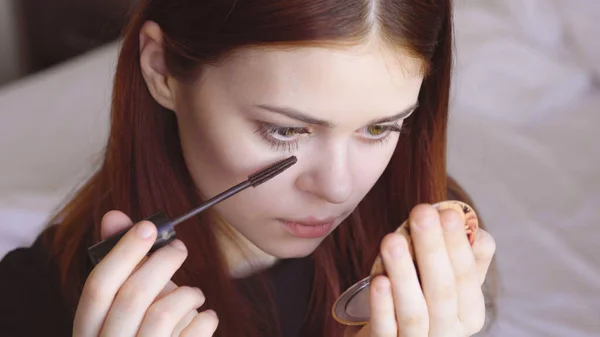 Frau malt Wimpern mit Spiegel in der Hand zur Selbstpflege Weiblichkeit — Stockfoto