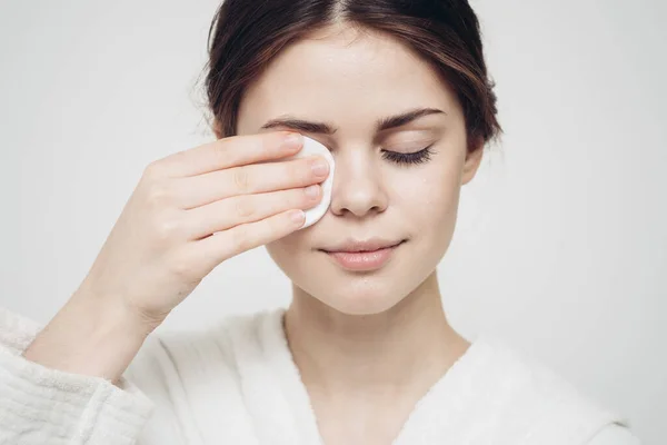 Vrouw in een badjas veegt haar gezicht met een witte spons uiterlijk zorg cosmetologie — Stockfoto