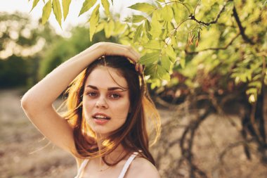 Doğada ağaçların yanında giyinmiş kızıl saçlı hoş bir kadın.