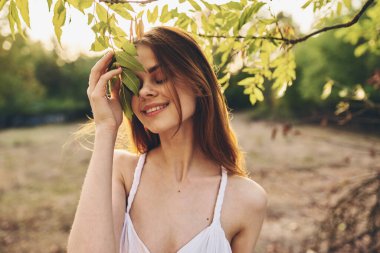 Doğadaki yeşil ağaçların yanında beyaz elbiseli romantik bir kadın.