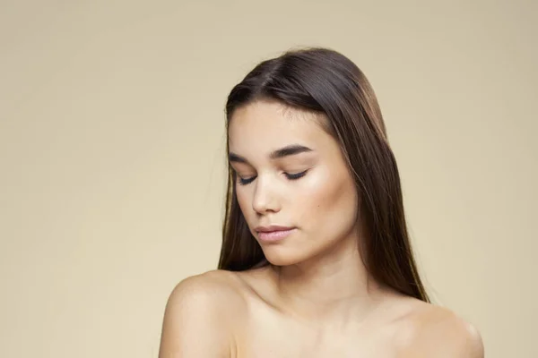Frau mit entblößten Schultern dunkle Haare saubere Haut Make-up beige Hintergrund — Stockfoto