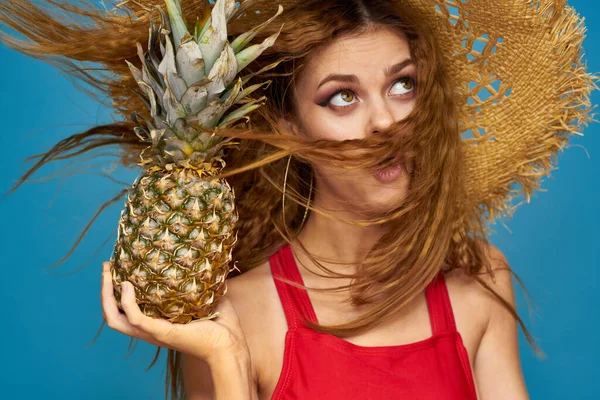 Kobieta w słomkowym kapeluszu z ananasem w rękach falowane włosy egzotyczne owoce można lato niebieski tło wakacje — Zdjęcie stockowe