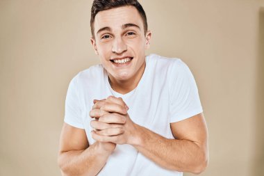 Duygusal adam beyaz tişörtlü, elleri yaşam tarzı bej arka planlı jestler