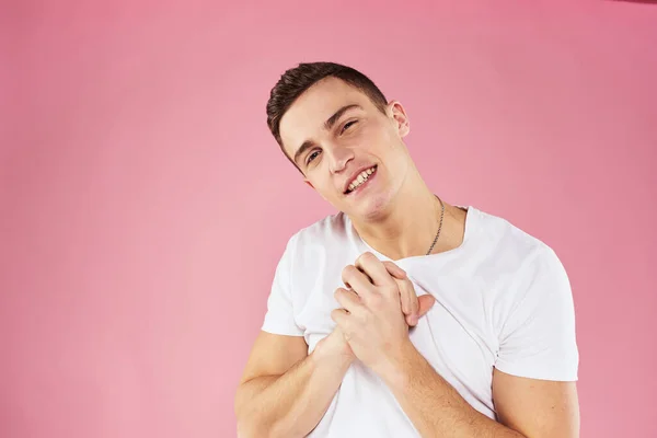 A man in a white t-shirt gestures with his hands emotions pink background studio cropped view — Stock Photo, Image