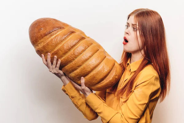 Emotional woman holding a loaf in a horizontal position on a light background and a yellow shirt — Stock Photo, Image