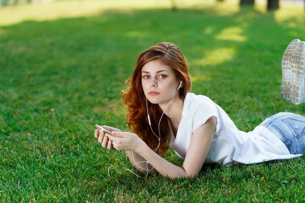 Hübsche Frau liegt auf dem Rasen im Park und hat Handy in der Hand — Stockfoto