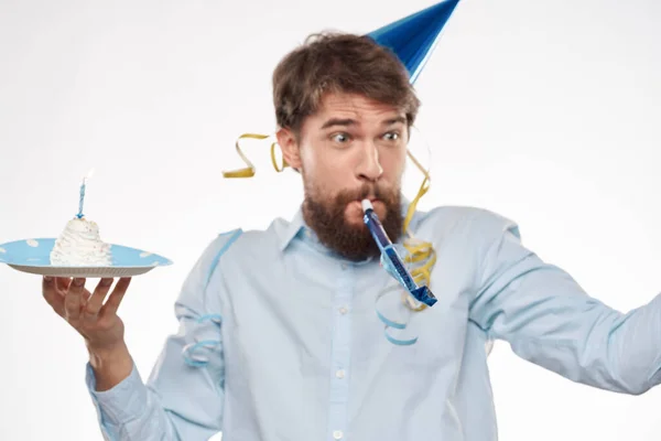 Mężczyzna świętuje urodziny na jasnym tle z tortem w czapeczce flet talerz zabawy — Zdjęcie stockowe