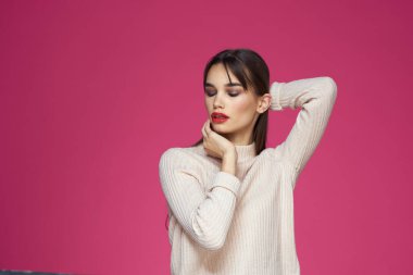 Uzun saçlı, kırmızı dudaklı beyaz bluzlu, pembe arka planlı çekici bir kadın.