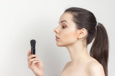 Elinde fırçayla esmer, makyajlı cilt bakımı yapıyor.