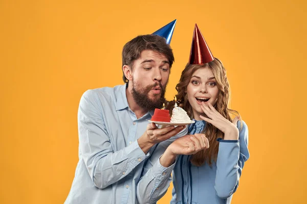 Anniversaire fête homme et femme dans une casquette avec un gâteau sur un fond jaune vue recadrée — Photo