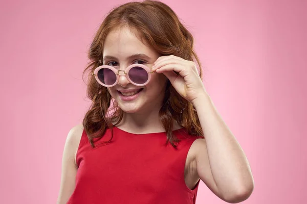 쾌활 한 어린 소녀어린 시절검은 안경을 쓴 빨간 드레스를 입은 핑크 색 배경 — 스톡 사진