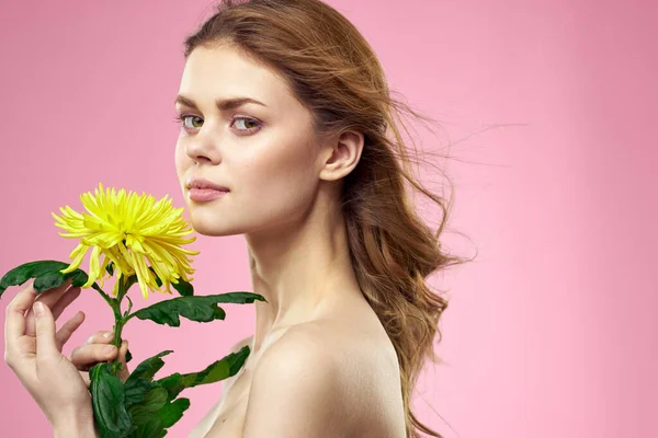 Hermosa chica con una flor amarilla sobre un fondo rosa maquillaje hombros desnudos — Foto de Stock