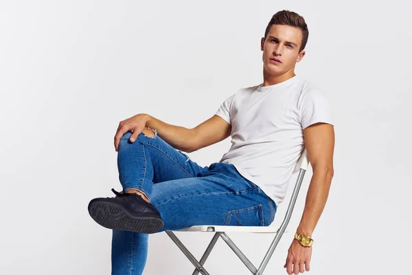 Homme sur une chaise intérieur déchiré jeans blanc t-shirt beau visage modèle fond clair — Photo