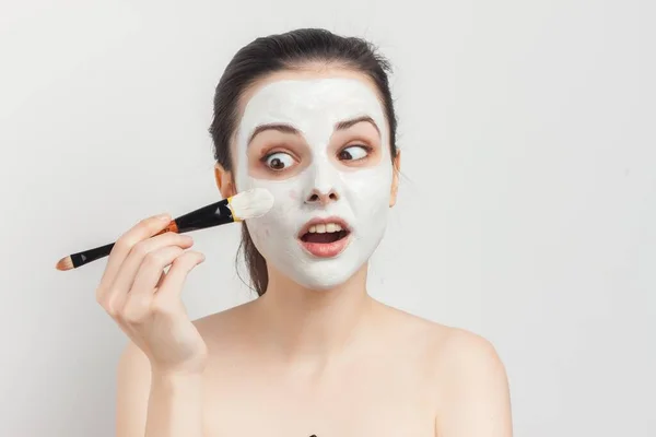 Женщина с голыми плечами наносит макияж кистью на лицо — стоковое фото