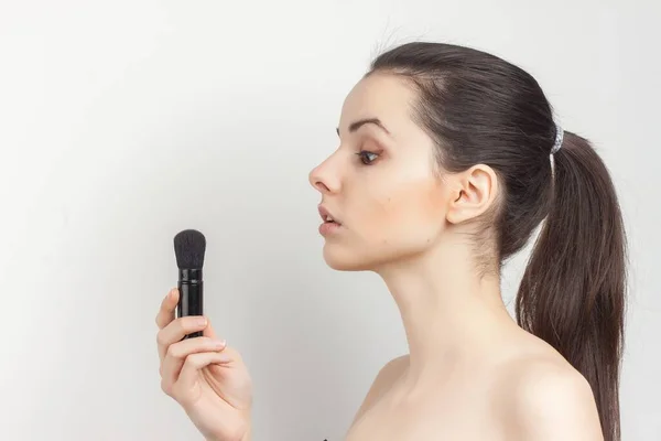 Brünette mit einem Pinsel in den Händen, der Make-up aufträgt — Stockfoto
