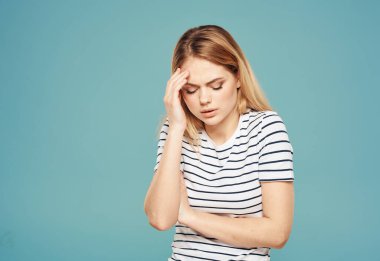 Kafası karışmış bir kadın, mavi bir arka plan modeli üzerinde elleriyle yüzüne dokunuyor. Stres duyguları.