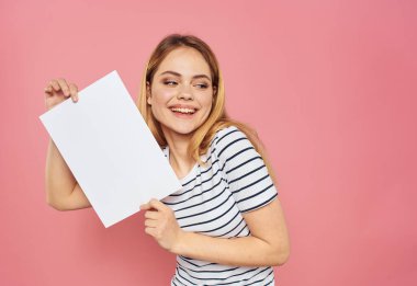 Pembe bir arka plan modeli üzerinde beyaz bir kağıt tabakası olan güzel sarışın kadın.
