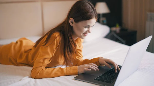 Vrolijke vrouw in de slaapkamer ligt op het bed voor de laptop communicatie — Stockfoto