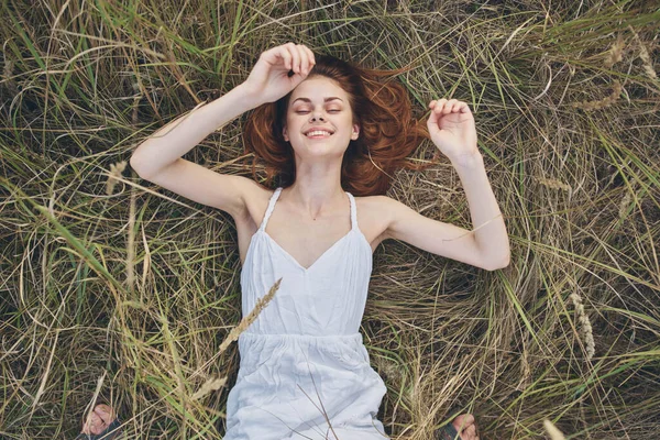 Gelukkig vrouw ligt op droog gras en gebaren met haar handen wit jurk kopiëren ruimte — Stockfoto