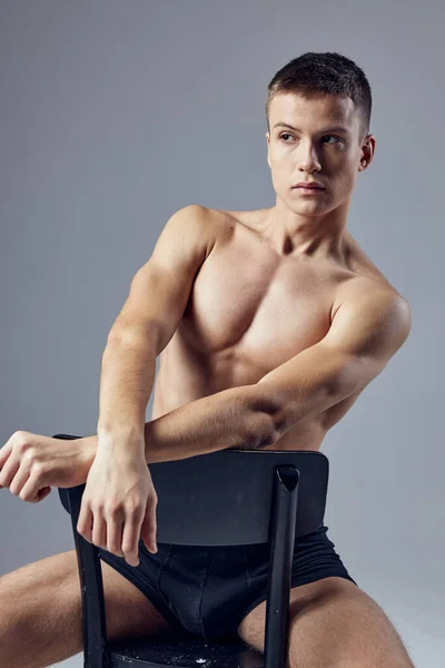 Homem bonito em shorts pretos físico atlético sentado em uma cadeira posando — Fotografia de Stock