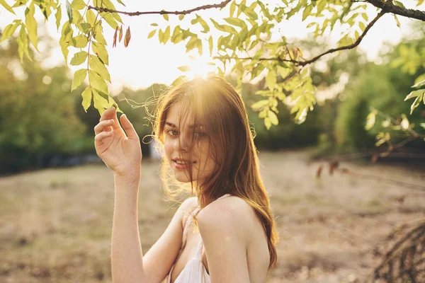 Romantische vrouw in witte jurk in de buurt van groene bladeren van bomen in de natuur — Stockfoto