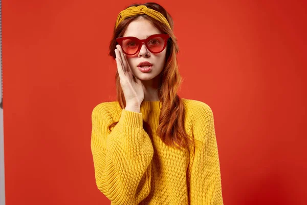 Jolie femme en pull jaune lunettes rouges vêtements à la mode close-up fond rouge — Photo