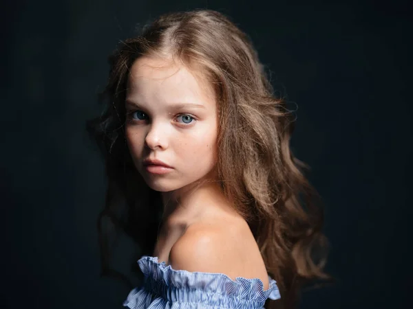 Retrato de una hermosa chica con el pelo rizado sobre un fondo oscuro, hombros desnudos y un vestido azul — Foto de Stock