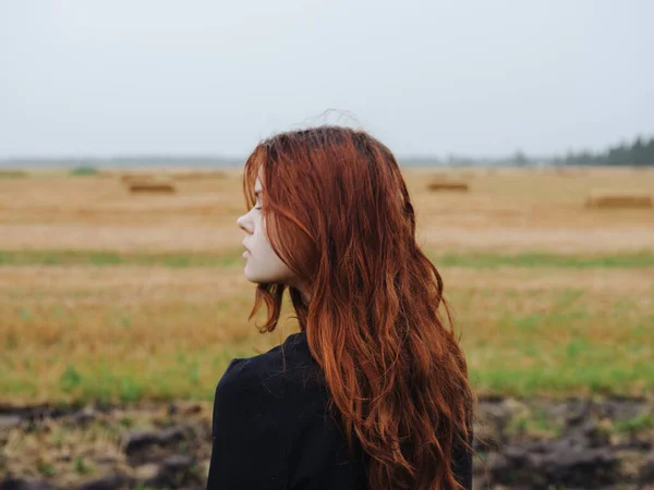 Portrait d'une femme aux cheveux roux vêtue d'une robe noire dans un champ en pleine nature vue dégagée — Photo