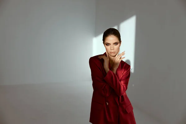 a woman with bright makeup and a red jacket In a dark room and a bright light from the window