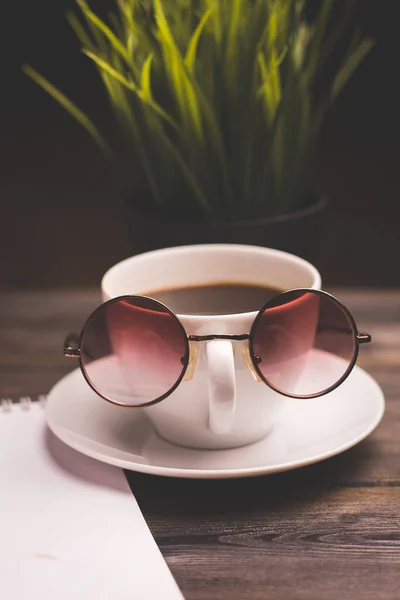 Taza de café con vasos en un platillo y una flor de mesa de madera en una olla en el fondo —  Fotos de Stock