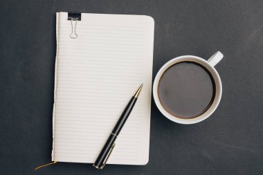 Koyu arka planda kalem ve bir fincan kahve ofisi manzaralı defter.