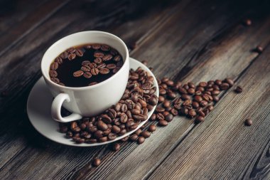 Kahve çekirdekli çay tabağı ve ahşap masa manzaralı beyaz bardak. Boşluğu kopyala.