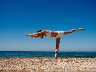 Mayo giymiş bir kadın doğa sahili manzarasında egzersiz yapıyor.