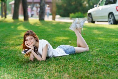 Güzel bir kadın bahçede uzanıyor. Telefonu elinde tutuyor.