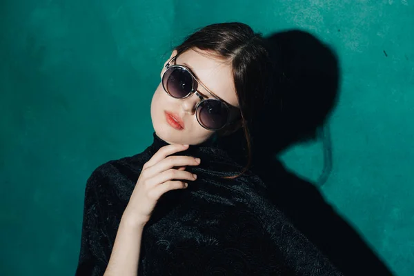 Mujer romántica en gafas y en un suéter negro sobre un fondo verde gestos con las manos — Foto de Stock