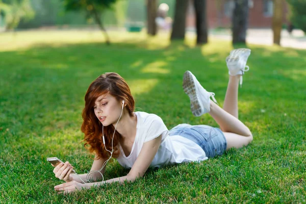 Mujer se encuentra en el césped al aire libre en el parque resto de teléfono en las manos —  Fotos de Stock