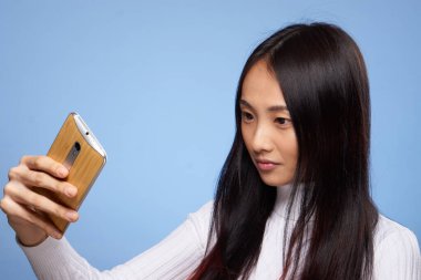 Asyalı görünümlü kadın elinde telefonla internet iletişim teknolojisi mavi arka planda.