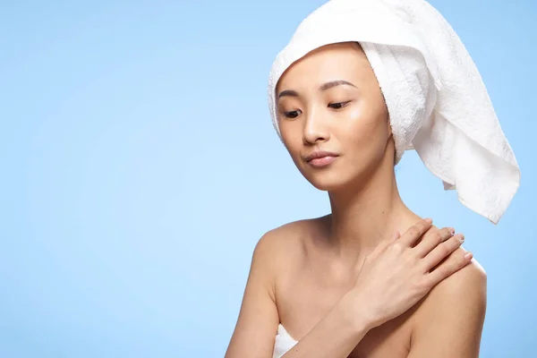 Vacker kvinna nakna axlar asiatiska utseende handduk på huvudet blå bakgrund — Stockfoto