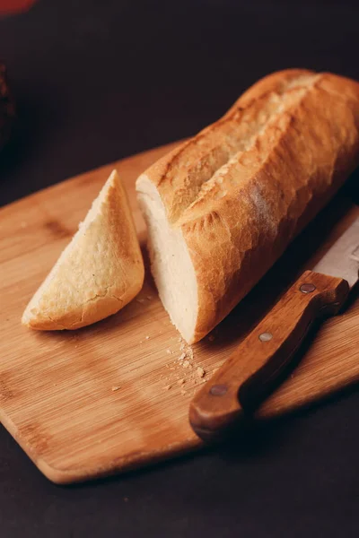Um pão fatiado em uma tábua e bolos assados fundo escuro — Fotografia de Stock