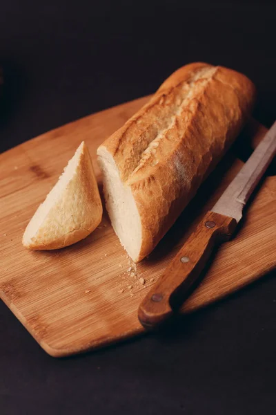 La hogaza del pan cortado sobre la tabla y la cocción los productos horneados el fondo oscuro —  Fotos de Stock