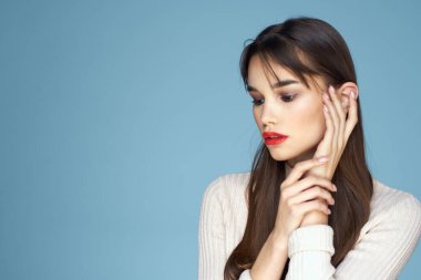 Beyaz süveterli esmer, kırmızı dudaklı, mavi manzaralı.