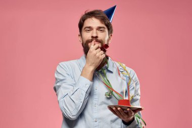 Pastalı ve mavi gömlekli bir adam pembe arka planda doğum günü tatili manzaralı.
