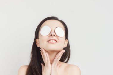 Çıplak omuzlu çekici esmer, süngerleri yüzünün yakınında tutuyor. Temiz bir ten.