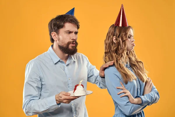 Aniversário festa homem e mulher em um boné com um bolo em um fundo amarelo vista cortada — Fotografia de Stock