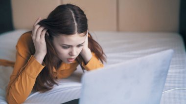 Duygusal kadın dizüstü bilgisayarın önünde yatakta uzanıyor. Serbest hoşnutsuzluk.